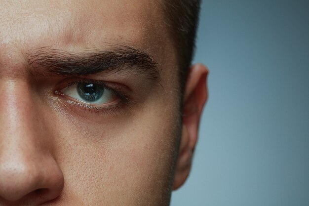 Close-up ritratto di giovane uomo isolato su grigio di sfondo per studio. Il viso e l'occhio azzurro del modello maschio caucasico. Concetto di salute e bellezza maschile, cura di sé, cura del corpo e della pelle, medicina o fisiologia.