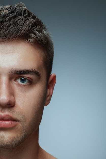 Close-up ritratto di giovane uomo isolato su grigio di sfondo per studio. Modello maschio caucasico che guarda l'obbiettivo e in posa, sembra serio. Concetto di salute e bellezza maschile, cura di sé, cura del corpo e della pelle.