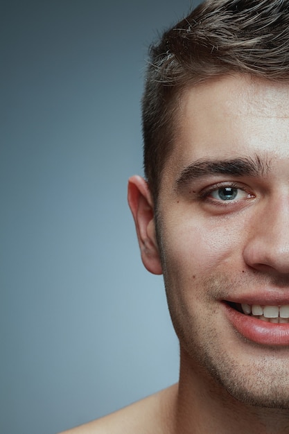 Close-up ritratto di giovane uomo isolato su grigio di sfondo per studio. Modello maschio caucasico che guarda l'obbiettivo e posa, sorridente. Concetto di salute e bellezza maschile, cura di sé, cura del corpo e della pelle.