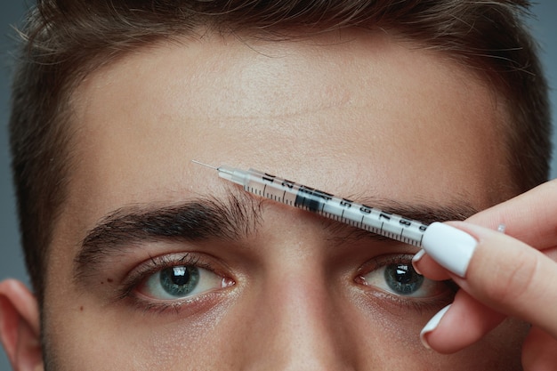 Close-up ritratto di giovane uomo isolato su grigio di sfondo per studio. Procedura di chirurgia di riempimento. Concetto di salute e bellezza maschile, cosmetologia, cura di sé, cura del corpo e della pelle. Anti età.