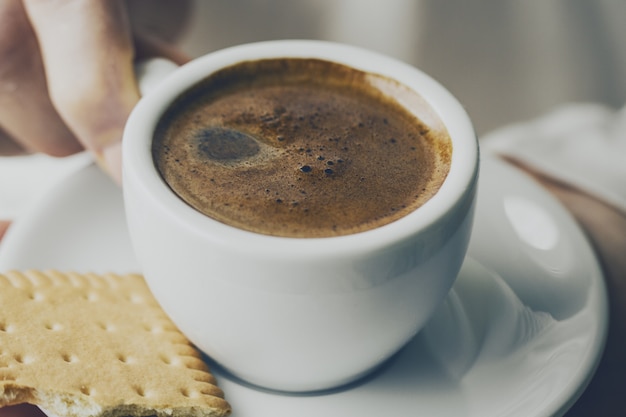 Closeup di gustoso caffè espresso con gustoso schiuma in piccola tazza di ceramica. Mani femminili in possesso di bevanda calda calda.