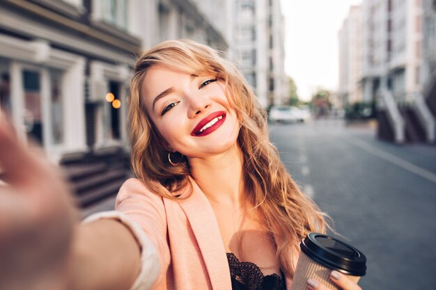 Closeup selfie-ritratto bella ragazza bionda sulla strada in città. Ha labbra vinose