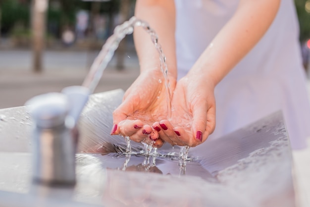 Closeup sulla donna che cattura acqua. Spruzzi gocce su sfondo estivo di estate all&#39;aperto. Concetto di ambiente e salute. Fontana fluente bevanda fredda