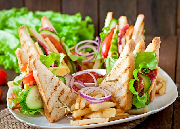 Club sandwich con formaggio, cetriolo, pomodoro, carne affumicata e salame. Servito con patatine fritte.