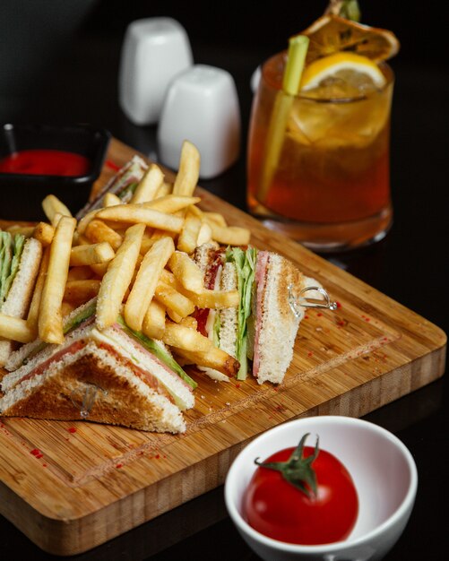 Club sandwich con patate su una tavola di legno con pomodoro e limonata.