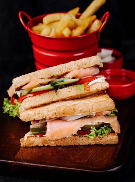 Club sandwich con verdure e prosciutto, con patatine fritte.