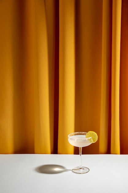 Cocktail della calce in vetro del piattino sulla tavola bianca contro la tenda gialla
