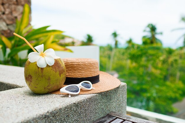 Cocktail di cocco decorato plumeria, cappello di paglia e occhiali da sole sul tavolo.