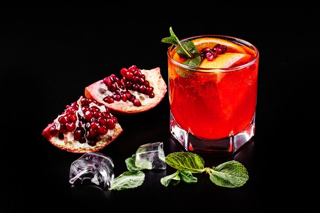 Cocktail di vodka, granatina, melograno, ghiaccio e menta si erge su un tavolo nero