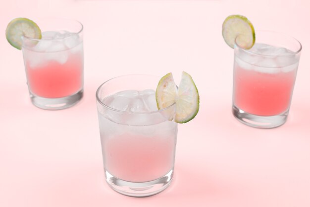 Cocktail fresco con cubetti di ghiaccio e fette di limone su sfondo rosa