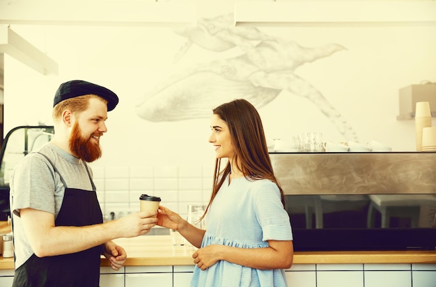 Coffee Business Concept Positivo giovane uomo barbuto e bella donna attraente barista coppia in grembiule guardando la fotocamera mentre si trova al bancone del bar