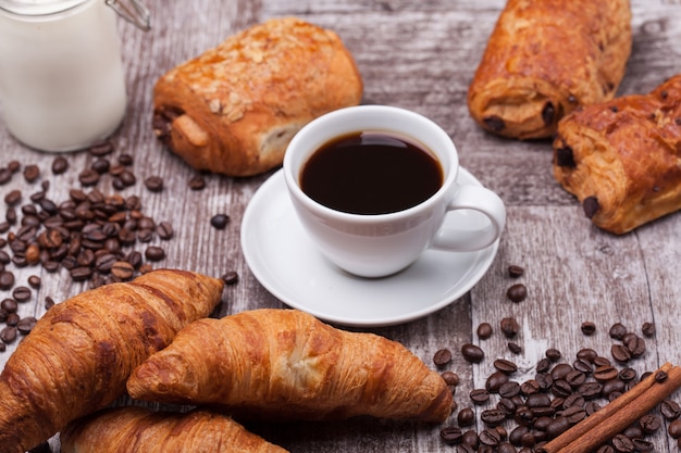 Colazione con coissants freschi con caffè e latte su tavola in legno rustico. Cornetto d'oro.