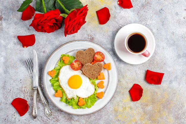 Colazione di San Valentino: uova fritte e pane a forma di cuore e verdure fresche.