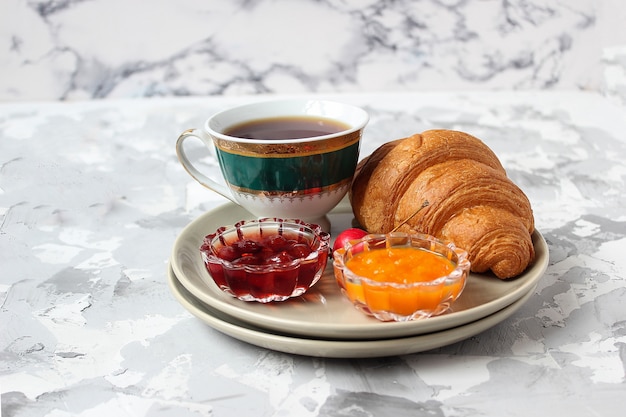 Colazione francese con cornetti, marmellata di albicocche, marmellata di ciliegie e una tazza di tè, fiori rossi e gialli