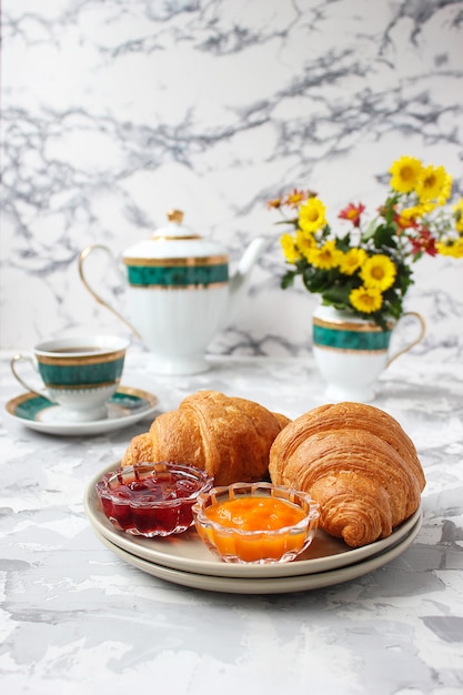 Colazione francese con cornetti, marmellata di albicocche, marmellata di ciliegie e una tazza di tè, fiori rossi e gialli