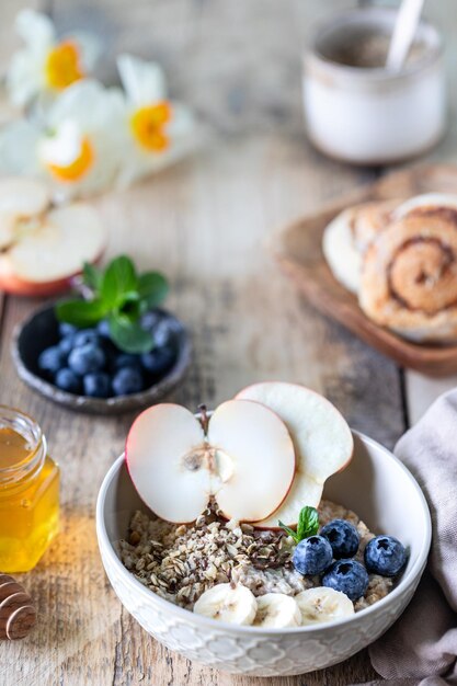 Colazione sana farina d'avena o muesli con mirtilli mela e miele su un fondo di legno rustico