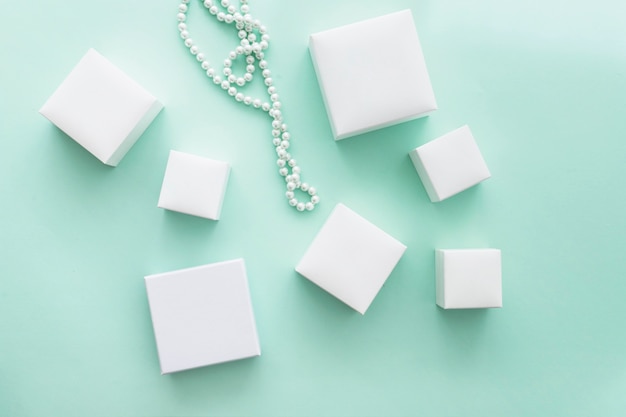 Collana di perle con diverse scatole bianche su sfondo turchese