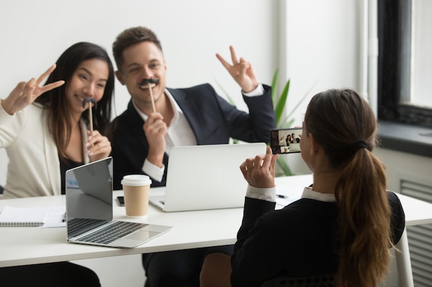 Collega che cattura maschera sullo smartphone dei colleghi con i baffi falsi