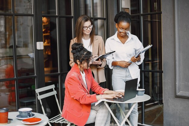 Colleghe che discutono i dati nella caffetteria all'aperto. Donne multirazziali che analizzano la strategia produttiva per la proiezione aziendale utilizzando documenti in street cafe