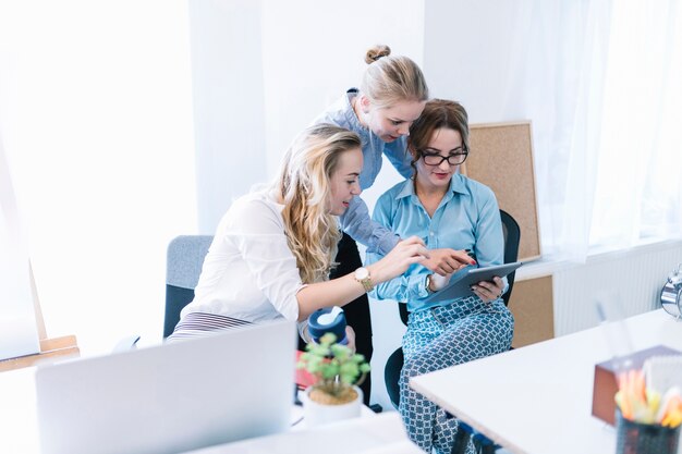 Colleghe femminili che indicano e che esaminano compressa digitale nell&#39;ufficio