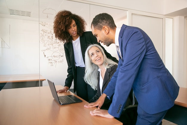 Colleghi amichevoli che discutono progetto nella stanza dell'ufficio e che sorridono. Riuscite imprenditrici di contenuto dai capelli grigi seduti a tavola e parlare con i partner. Concetto di lavoro di squadra, affari e gestione