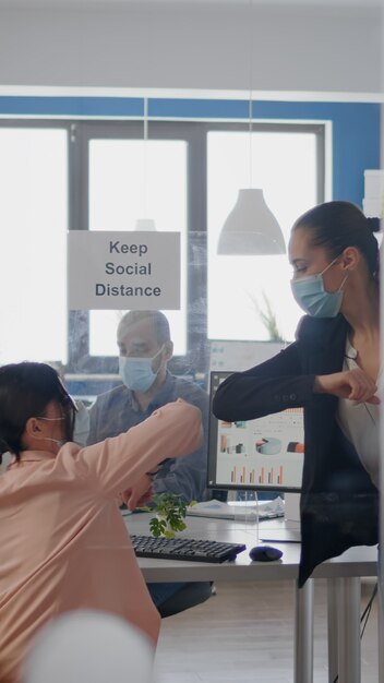 Colleghi che toccano il gomito per evitare l'infezione con il team aziendale del coronavirus che indossa una maschera medica...
