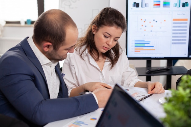 Colleghi di attività di avvio che discutono guardando i documenti nella sala conferenze di brainstorming del consiglio di amministrazione dell'azienda controllando grafici e grafici