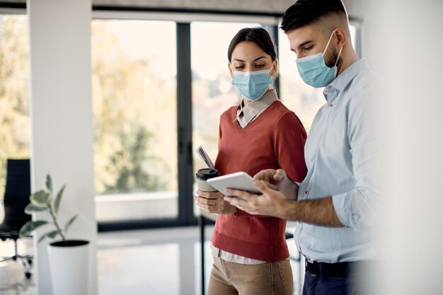 Colleghi di lavoro che indossano maschere facciali mentre lavorano sul touchpad in ufficio