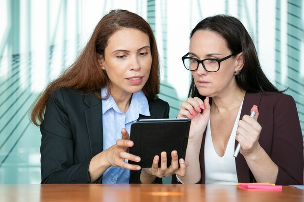 Colleghi femminili concentrati che guardano insieme il contenuto sul tablet, guardando lo schermo per l'eccitazione mentre è seduto al tavolo nella sala riunioni.