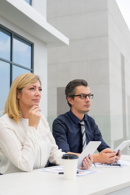 Colleghi pensierosi maschili e femminili che lavorano nel caffè all&#39;aperto.