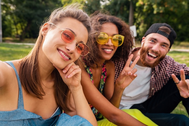 Colorato elegante felice giovane compagnia di amici seduti parco, uomo e donna che hanno divertimento insieme