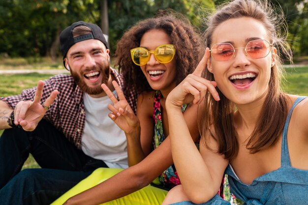 Colorato elegante felice giovane compagnia di amici seduti parco, uomo e donna che hanno divertimento insieme