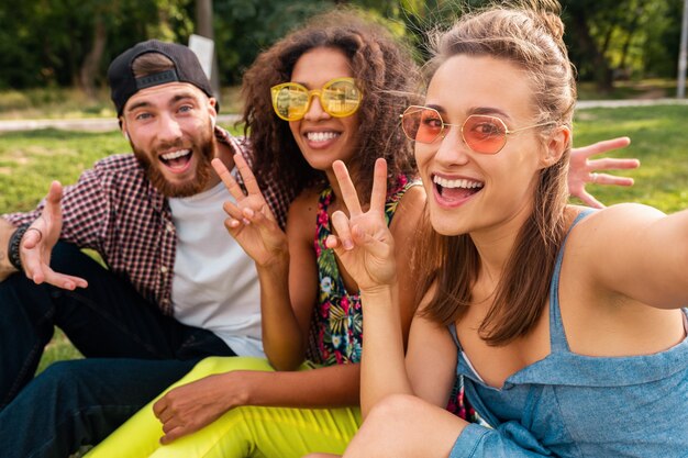 Colorato elegante felice giovane compagnia di amici seduti parco, uomo e donna che hanno divertimento insieme