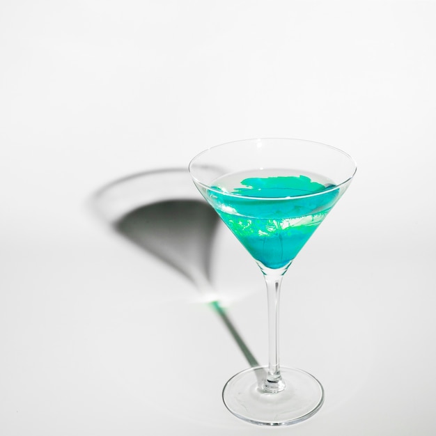 Colore turchese diffuso in acqua all&#39;interno del bicchiere da martini con ombra su sfondo bianco