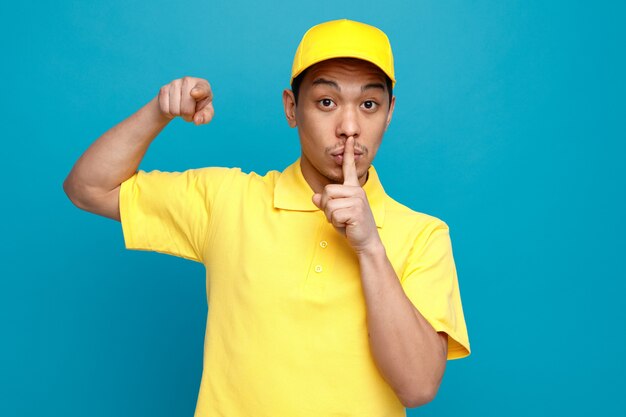 Colpito il giovane fattorino che indossa l'uniforme e il berretto che punta al lato facendo gesto di silenzio