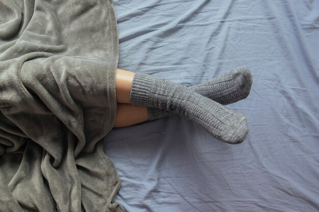Colpo ad alto angolo delle gambe di una donna in calzini grigi lavorati a maglia sotto la coperta