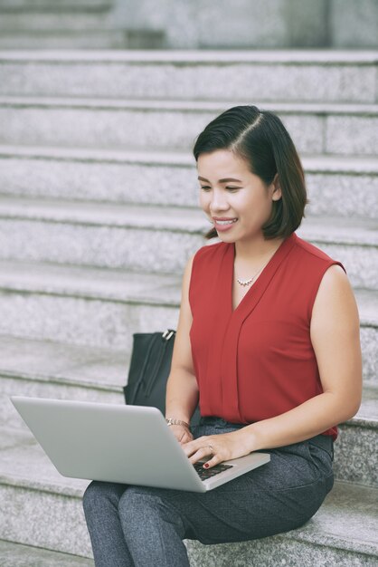 Colpo completo della donna attraente che per mezzo del computer portatile messo sulle scale all'aperto