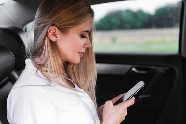 Colpo del primo piano con una donna bionda che esamina smarphone