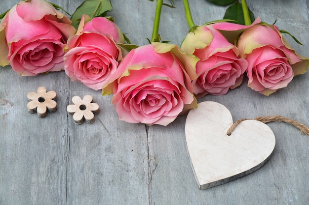 Colpo del primo piano dei fiori di rosa rosa con un'etichetta di legno del cuore con spazio per testo su una superficie di legno