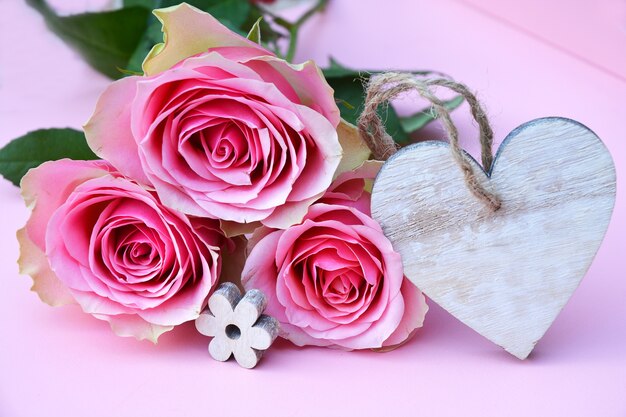 Colpo del primo piano dei fiori di rosa rosa con un'etichetta di legno del cuore con spazio per testo