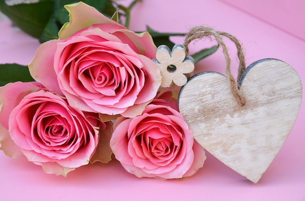 Colpo del primo piano dei fiori di rosa rosa con un'etichetta di legno del cuore con spazio per testo