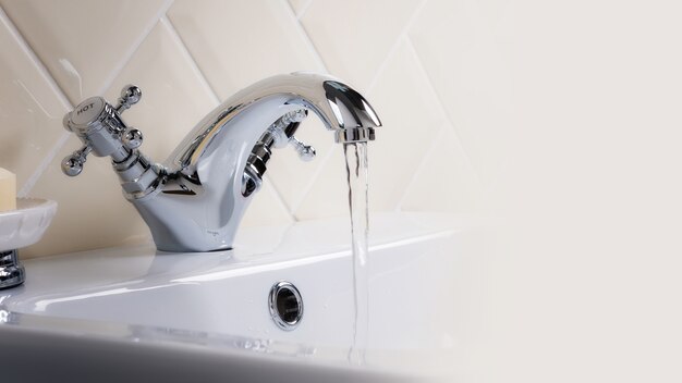 Colpo del primo piano dell'acqua che scorre da un miscelatore del lavabo in bagno