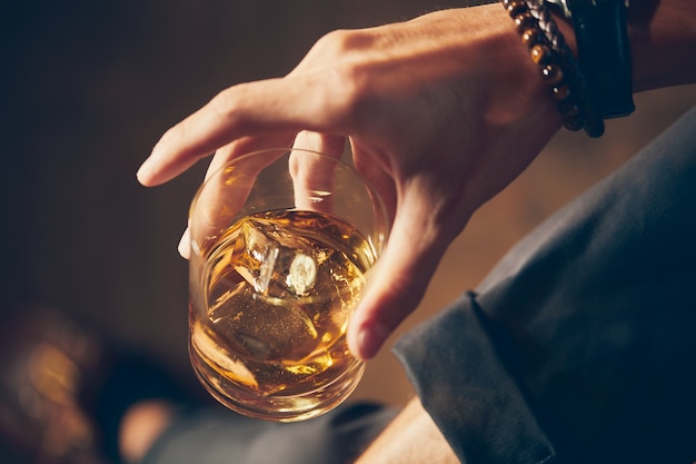 Colpo del primo piano dell'angolo alto di un maschio che tiene un bicchiere di whisky