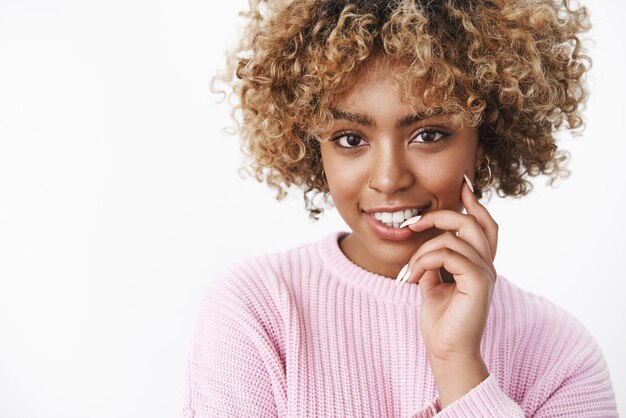 Colpo del primo piano della giovane donna afroamericana tenera civettuola e sexy con taglio di capelli ricci biondi che morde il dito sensualmente con il desiderio guardando la telecamera civettuola su sfondo bianco