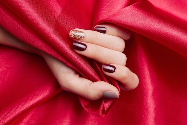 Colpo del primo piano della mano di una donna con un bellissimo smalto per unghie che accarezza un tessuto di seta rosso