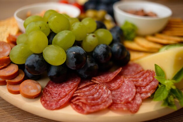 Colpo del primo piano delle fette di salame e dell'uva su un piatto da spuntino