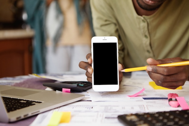 Colpo del primo piano delle mani dell'uomo dalla carnagione scura che tengono il telefono cellulare e che indica la matita alla sua schermata vuota