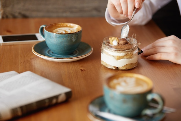 Colpo del primo piano delle mani della donna che mangia il dessert dolce con un cucchiaio