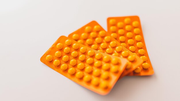 Colpo del primo piano delle pillole arancioni sui precedenti bianchi