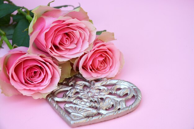 Colpo del primo piano delle rose rosa con una forma metallica del cuore su una superficie rosa